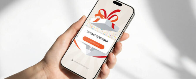Eine Hand hält ein Smartphone, auf dem eine Grafik einer Geschenkbox und der Text DU HAST GEWONNEN sowie die Schaltfläche ZUM GUTSCHEIN im Rahmen eines Masterclass-Gamification-Erlebnisses angezeigt werden.