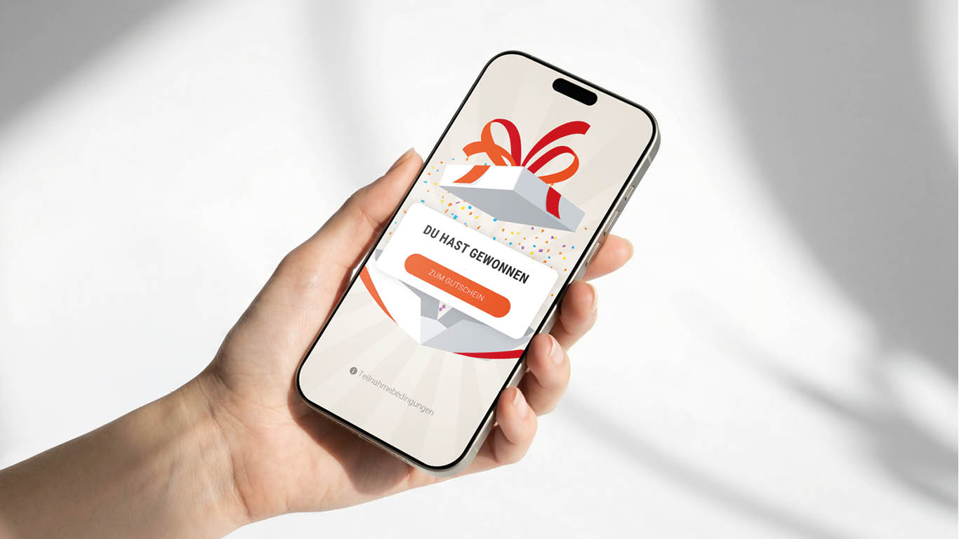 Eine Hand hält ein Smartphone, auf dem eine Grafik einer Geschenkbox und der Text DU HAST GEWONNEN sowie die Schaltfläche ZUM GUTSCHEIN im Rahmen eines Masterclass-Gamification-Erlebnisses angezeigt werden.